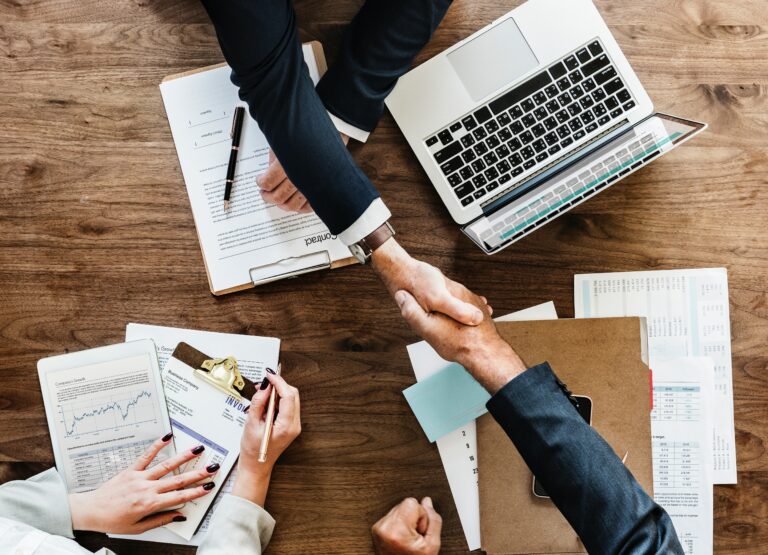 birds eye view of business people shaking hands over folders and laptop on wooden desk