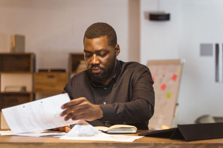 A black man wearing a black long sleeved shirt looking and reviewing papers.