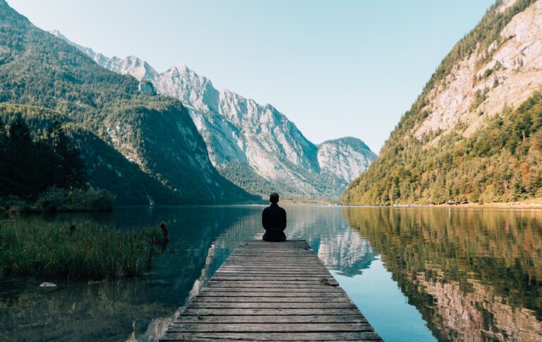 The man sitting on a dock in a valley on a lake.