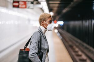 a black woman wearing a mask in professional clothing waiting for the subway.